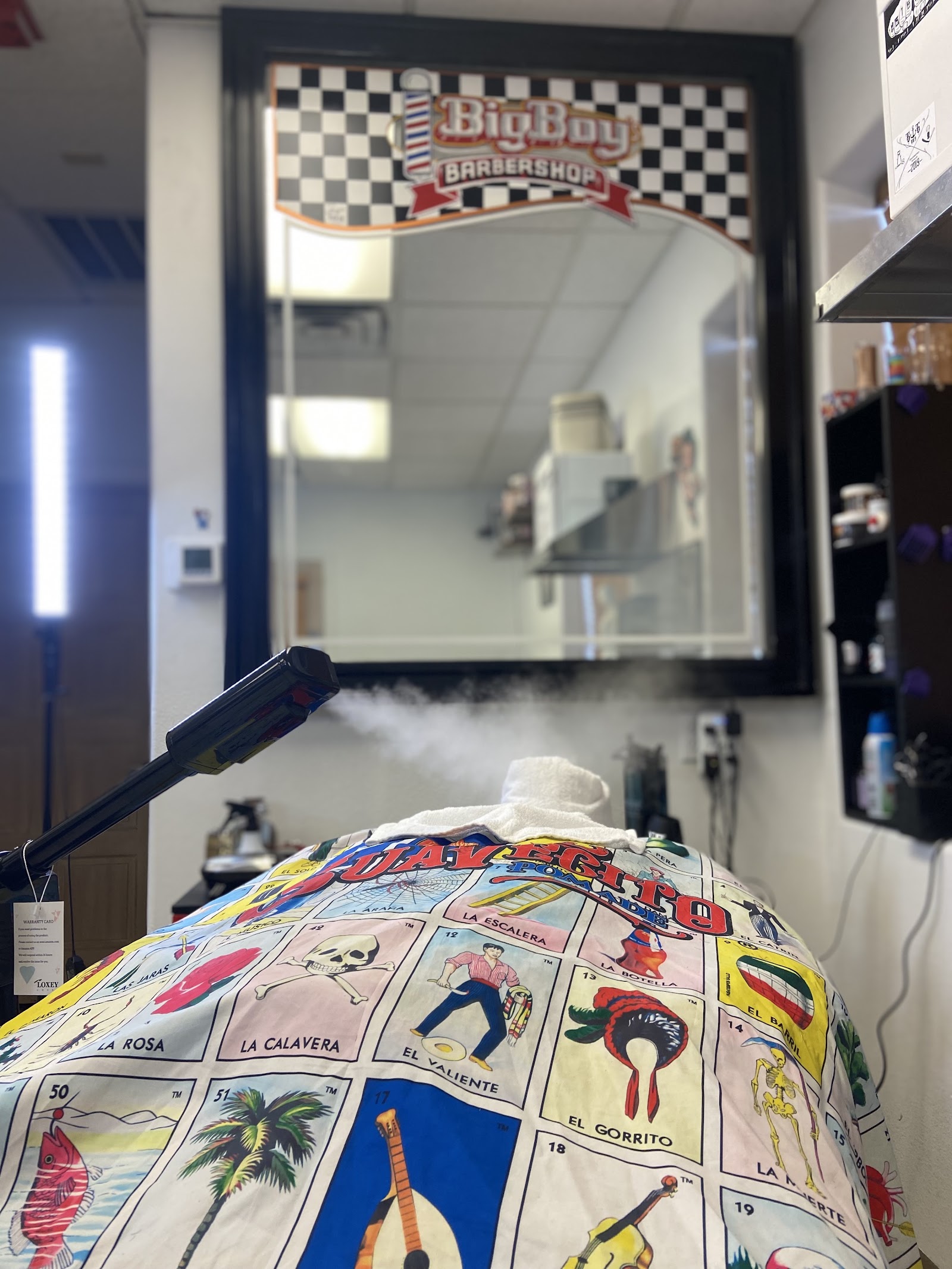 Barber station with a mirror bearing the Big Boy Barbershop logo and rising hot towel steam